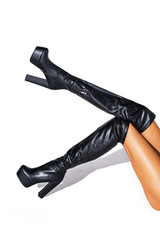 Raised up the feet of girls on whom beautiful shoes. Black hessian boots on the feet of a model on a white background with shadows. jackboots. studio shooting. thin legs. fashionable boots