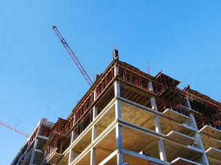 Construction site background. Concrete building under construction. Crane near building against blue sky.