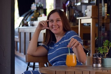 Sitting brunette woman in a striped dress in a cafe drinking orange juice.