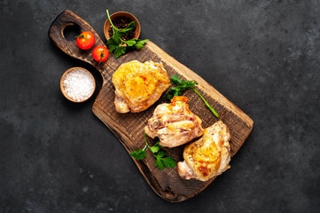 Grilled chicken thighs on a cutting board with spices on a stone background with copy space for your text