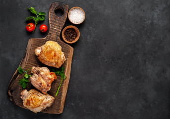 Grilled chicken thighs on a cutting board with spices on a stone background with copy space for your text
