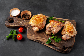 Grilled chicken thighs on a cutting board with spices on a stone background with copy space for your text