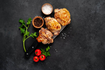 Grilled chicken thighs on a knife with spices on a stone background with copy space for your text