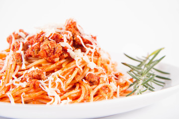 Spaghetti bolognese on a plate decorated with a rosemary twig and sprinkled with cheese