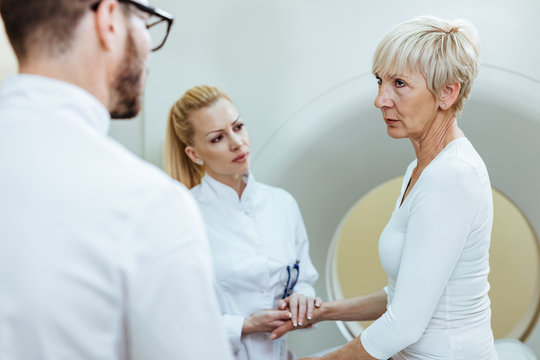 Distraught mature woman talking with doctors before MRI scan examination at clinic.