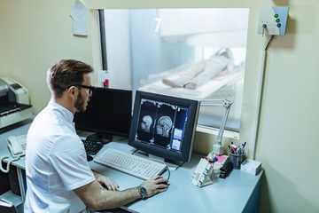 Fototapeta na wymiar Male radiologist analyzing MRI scan results of a patient on computer monitor in control room.