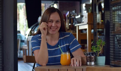 A woman in a striped dress is sitting in a cafe drinking orange juice.