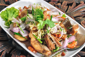 Fried Fish Salad in white plate on the wooden table.
