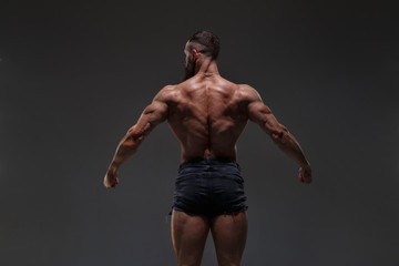 Fototapeta na wymiar Portrait of a athletic man with a naked torso showing muscles isolated on a dark gray background, view from the back.