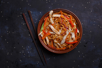Wok with chicken in kimchi sauce and teriyaki udon noodles in a brown bowl on the black surface.