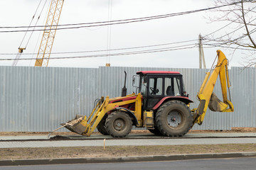 a tractor with two excavator buckets in front and behind on the sidewalk. excavator at a construction site on a background of a metal fence.