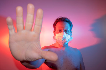  man with face mask shows stop sign with hand lit laterally by blue and red lights