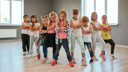 Dance team. Group of confident little girls keeping arms crossed, making serious faces and looking at camera while standing in the dance studio. Choreography class