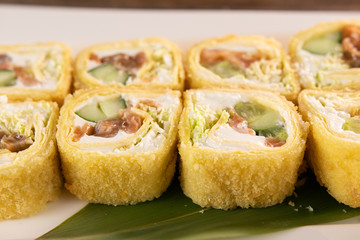 fried sushi rolls with salmon and cucumber on white plate close up