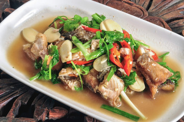 Fried fish with celery in white plate on the wooden table.