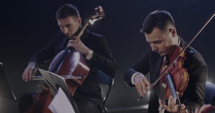 Male and female cellist and violists playing on instruments in orchestra together at concert. Symphony musicians rehearsing. Orchestral art concept.