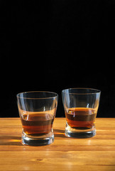 Two glasses of whiskey on a wooden table. Black background.
