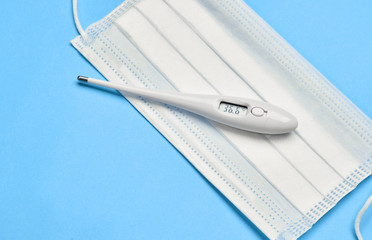 Medical thermometer and surgical mask on a blue background.