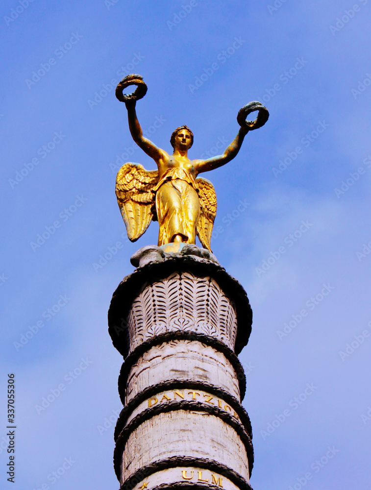 Wall mural The figure of an angel with wings gold color on the top of the column on the background of blue sky in the Paris area