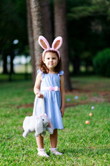 Little toddler girl with bunny ears. Easter egg hunt. - 337055726