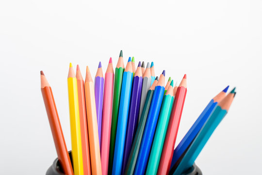 Group of many mixed colourful pencils in a black box isolated on a white table, children school or office suppliers photographed with soft focus from side view, with space for text
