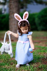 Little toddler girl with bunny ears. Easter egg hunt. - 337056104