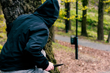 Mężczyzna z nożem schowany za drzewem - obrazy, fototapety, plakaty