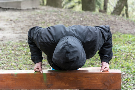 Mężczyzna w kapturze robi pompki na zewnątrz