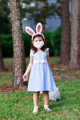 Little toddler girl with bunny ears and surgical face mask hunting for Easter eggs during coronavirus quarantine - 337056598