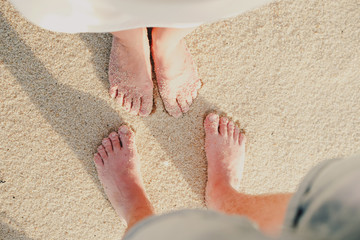 Legs of a guy and a girl stand opposite each other on the sand. Above view. He and she concept. Love and togetherness
