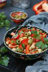 Healthy salad of chickpea, green olives, pepper and parsley located on wooden board on a dark background, Vertical format