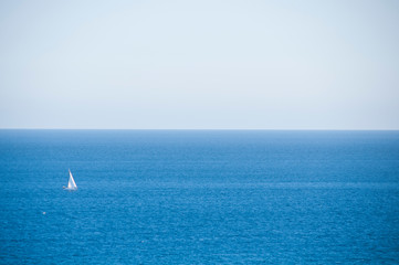 Obraz premium Lone white sailboat on a stretch of a bright blue sea. Sunny day. Mediterranean sea.