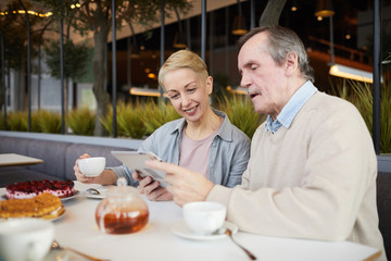 Fototapeta na wymiar Smiling mature couple watching something on digital tablet while drinking tea in the restaurant