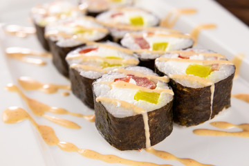 Sushi rolls with bell pepper and salmon poured with sauce on a white plate