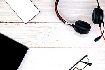 Tablet, Mobile phone, Glasses and Head set on white wooden table for work from home concept.