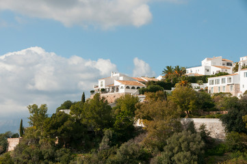 Fototapeta na wymiar White spanish village on a green hill. White spanish houses surrounded by greenery against a blue sky. Mediterranean architecture.