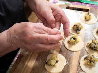 Senior woman is preparing a popular dish of dumplings with potatoes and mushrooms.