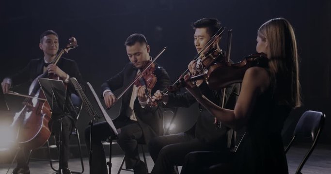 Professional multiethnic symphony orchestra playing on violins and cello at concert. Male and female musicians play on stage in theater. Asian and Caucasian virtuosos. Classical art concept.
