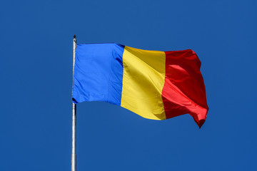 Romanian national flag blowing in the wind in direct sunlight towards clear blue sky
