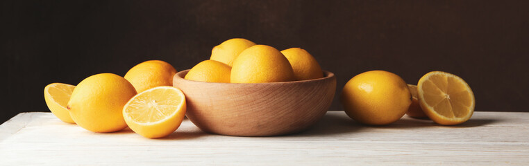 Wooden bowl and lemons against brown background, space for text