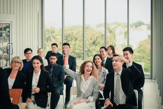 Group of business people sitting on conference together listening to the speaker giving a speech in the meeting room seminar, young woman raising hand up to ask question