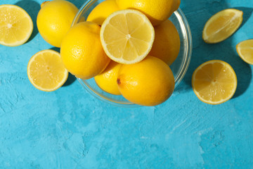 Bowl with lemons on blue background, top view. Ripe fruit