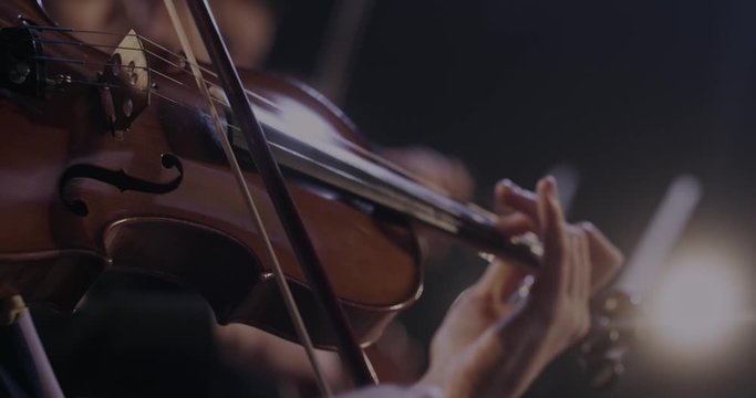Close up of violin in hands of Caucasian woman while she performing in classical orchestra. Female violinist playing on instrument at concert.