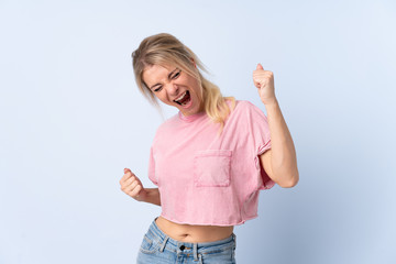 Blonde woman over isolated blue background celebrating a victory