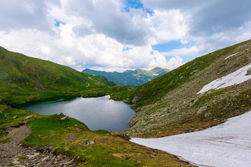 goat lake in the fagaras mountains of romania. popular travel destination. summer nature scenery with green grass and snow. ridge in the far distance beneath a cloudy sky