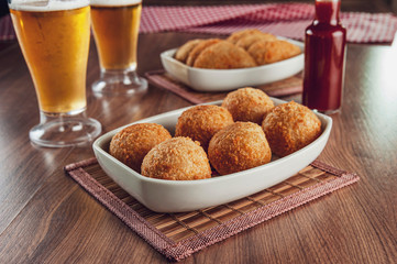 Brazilian appetizer deep fried cheese croquette with two glasses of beer and chilli sauce - Bolinha de queijo