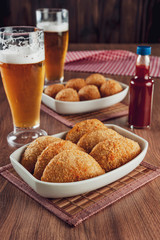 Brazilian appetizer deep fried beef croquette with two glasses of beer and chilli sauce - Risolis de carne