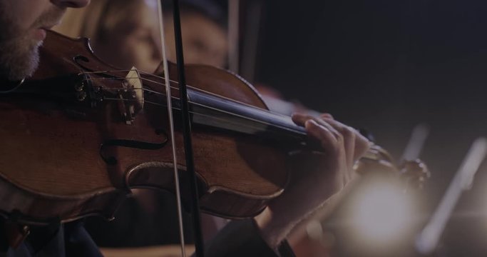 Close up of violin in hands of Caucasian man while he performing in classical orchestra. Male violinist playing on instrument at concert. Virtuoso concept. Classic band performance.