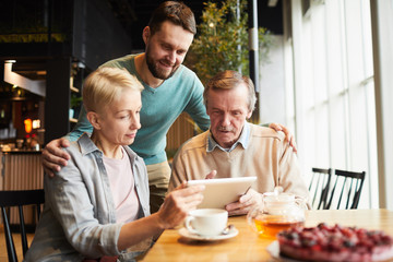 Mature parents and their son using digital tablet for online conversation while drinking tea in the restaurant