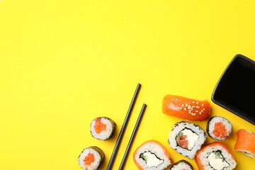 Sushi rolls, chopsticks and soy on yellow background, top view